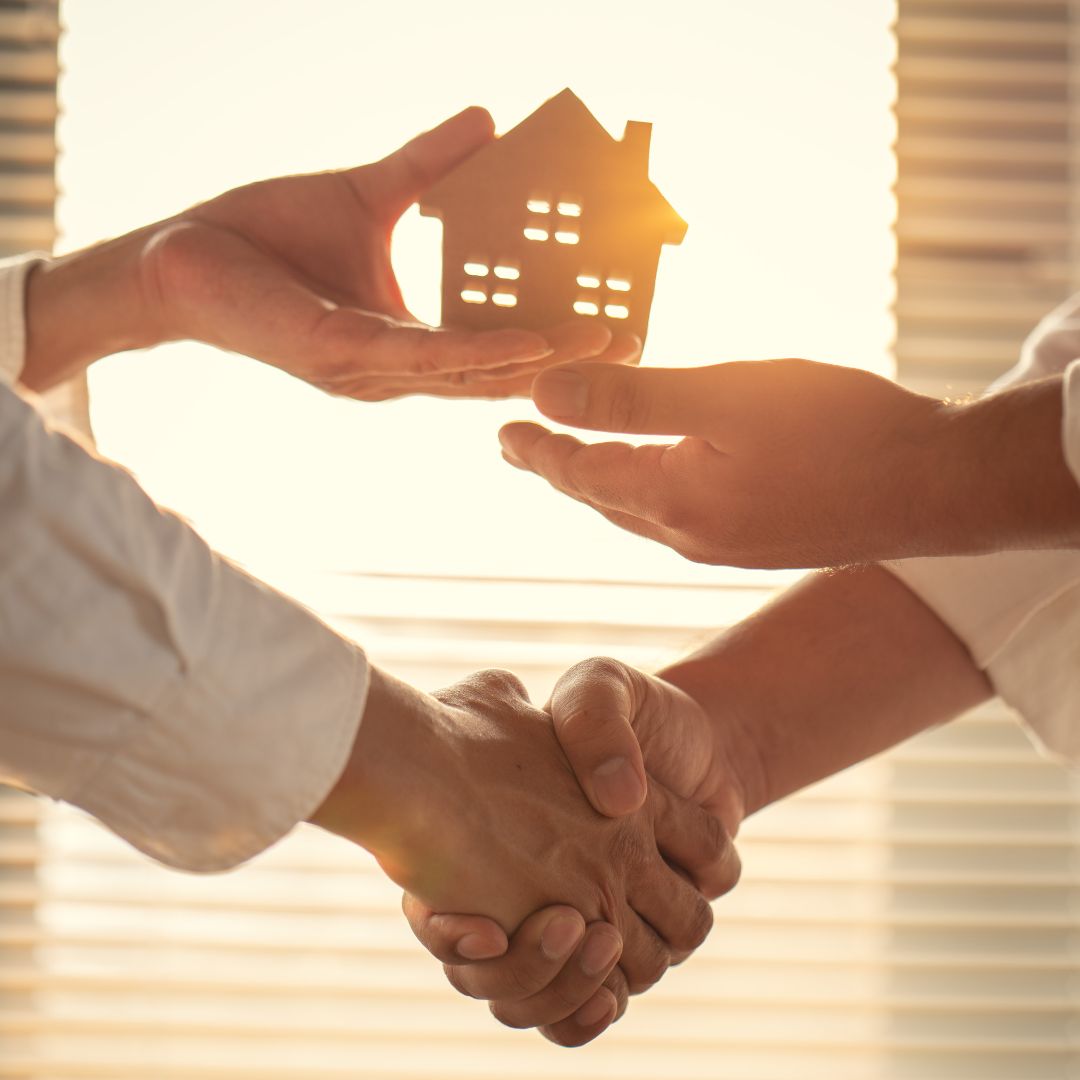 shaking hands and holding wood cutout of a house